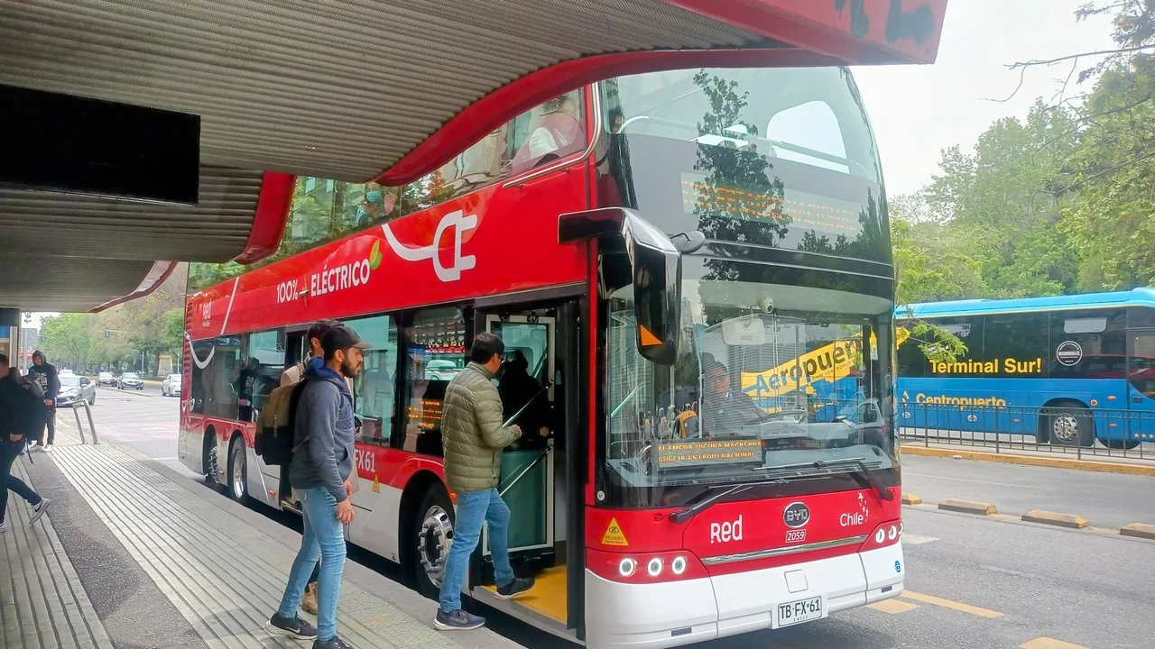 Autobús rojo de dos pisos de Red Metropolitana, con la leyenda 100% eléctrico, detenido junto a la acera en la Alameda de Santiago. Imagen de archivo del 30 de octubre de 2023; no muestra cargadores.
