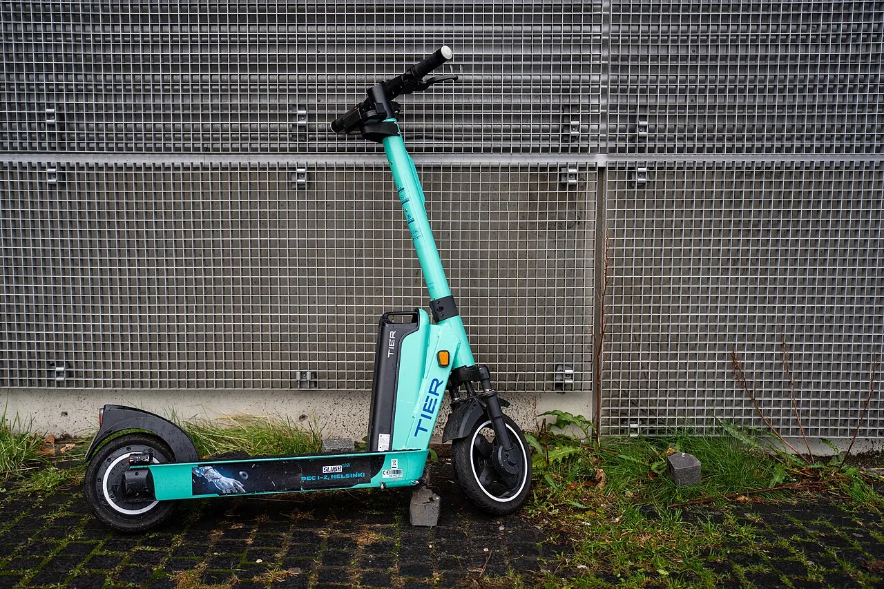 Patinete eléctrico TIER turquesa estacionado junto a una reja en Helsinki, Finlandia; fotografía de 2021.
