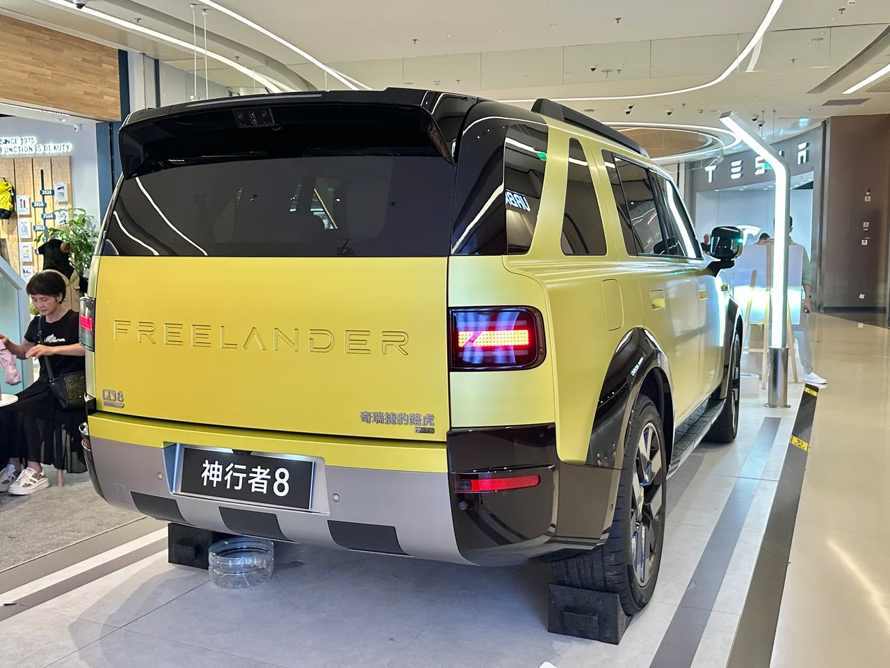 Rear three-quarter view of a yellow FREELANDER 8 display vehicle indoors in China-market context; Chinese text appears on its plate.