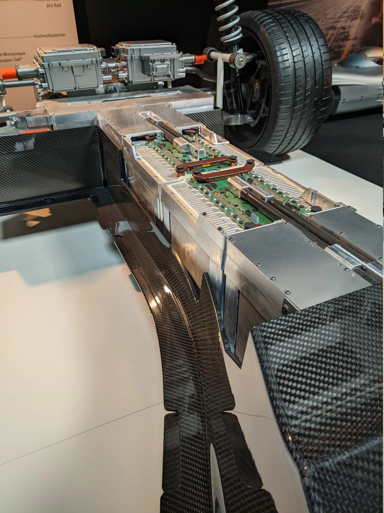 Conjunto de bateria instalado sob o assoalho de um veículo elétrico, com componentes eletrônicos e uma roda expostos.