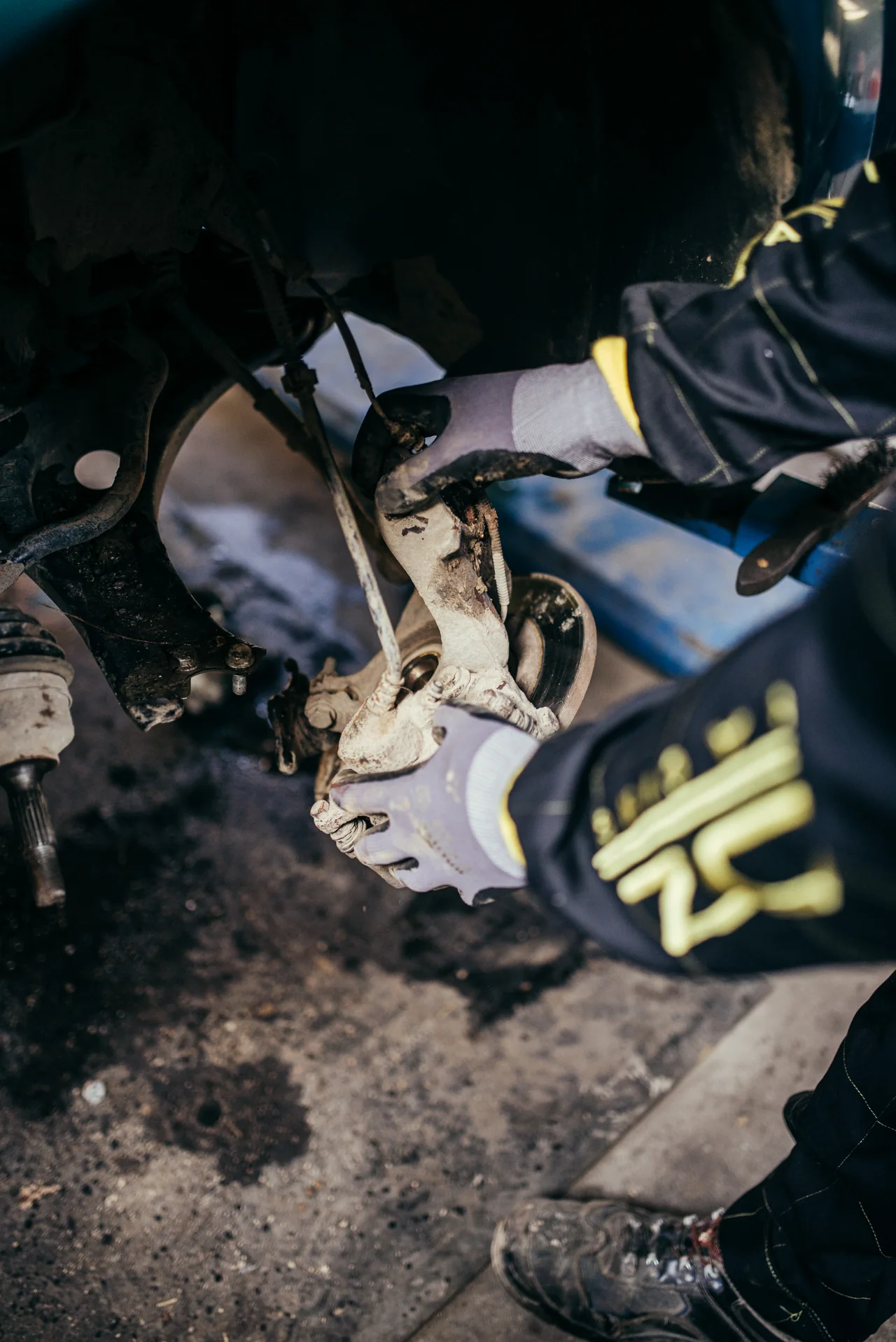 Mecánico con guantes trabaja en un componente situado bajo un automóvil; imagen de archivo de 2020.