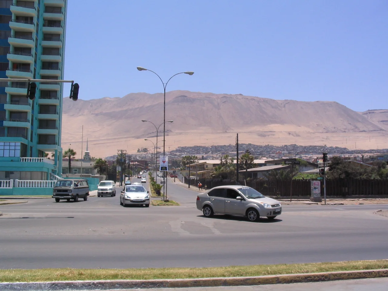 Vista de una avenida de Iquique con automóviles, edificios y cerros áridos al fondo.