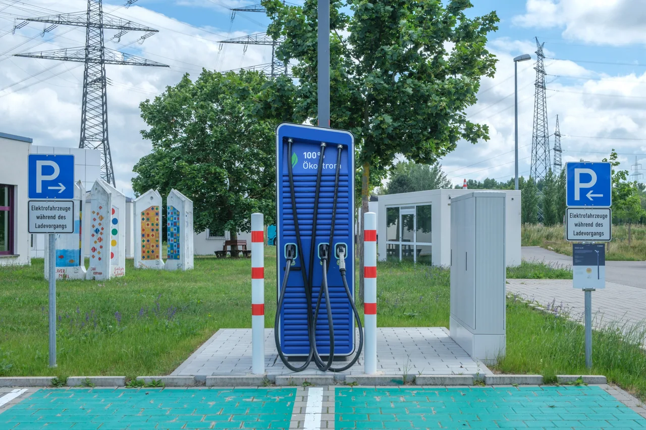 Carregador público azul para veículos elétricos com cabos e placas em alemão reservando vagas durante a recarga.