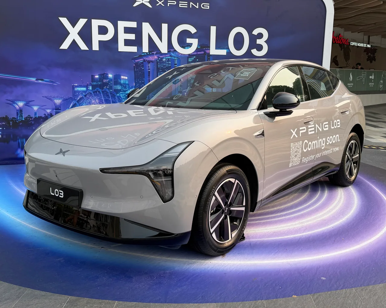 A white XPENG L03 show car at a Singapore display, with XPENG L03 graphics behind it.